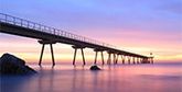 A long jetty, viewed from water level at dusk, stretches into the sea.
