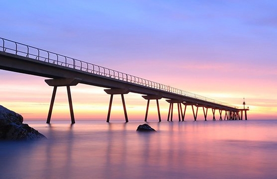 A long jetty, viewed from water level at dusk, stretches into the sea.