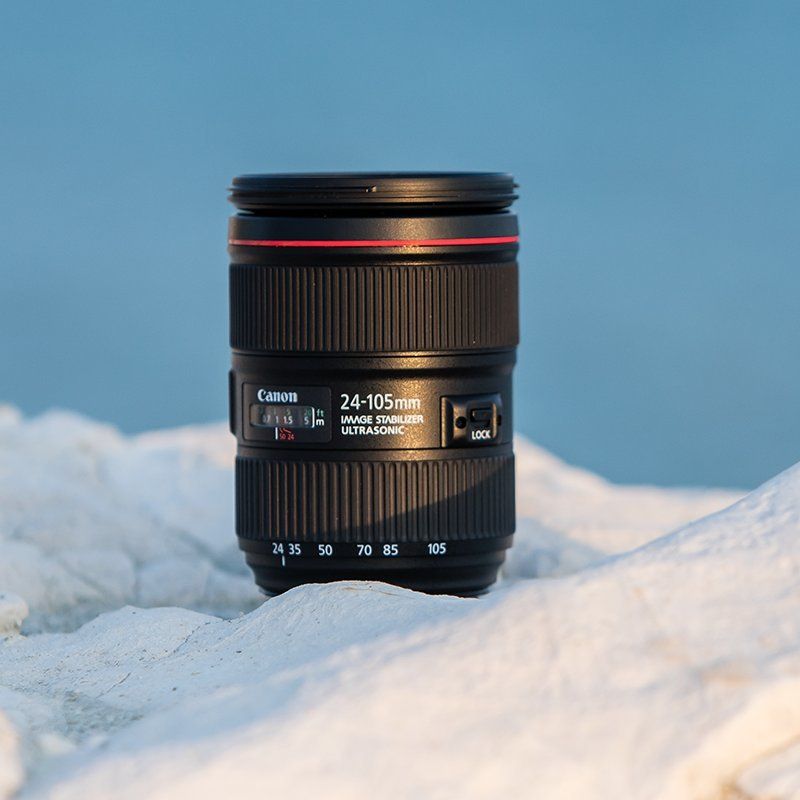 Canon lens EF 24-105mm f4L IS II USM placed amongst the snow with blue sky in the background.