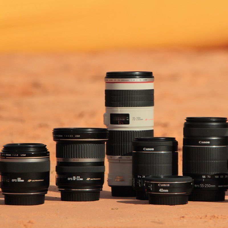 Several Canon lenses on the sandy ground.
