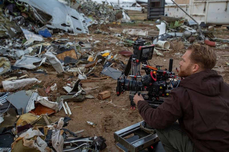 A cinematographer films with a Canon EOS C300 Mark III in a junkyard strewn with debris.