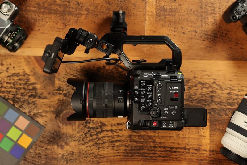 A Canon EOS C400 with an RF lens sits on a wooden table, surrounded by other camera lenses and products. 