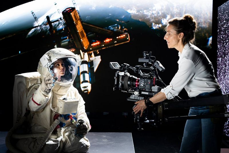 Cinematographer Sarah Thomas Moffat holds the Canon EOS C400 to film a woman in a space suit, with a satellite in the background.
