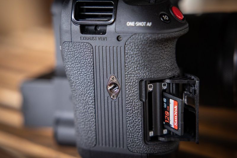 A close-up of a Canon EOS C70 camera showing a SanDisk card being inserted in one of two card slots. 