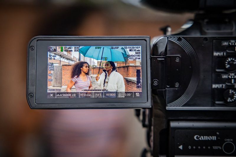 A close-up of the LCD screen of a Canon EOS C70 showing two people being filmed and the settings used.