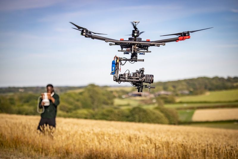 A Canon EOS C70 camera attached to a drone flying over a wheat field.