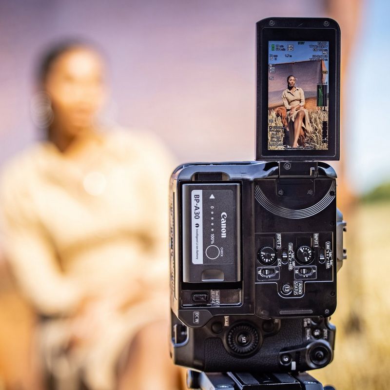 A Canon EOS C70 camera mounted vertically to film a seated woman in portrait mode.