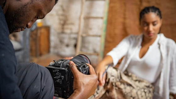 Jolade Olusanya holds a Canon EOS C70 camera to film a woman seated on the floor in front of him.