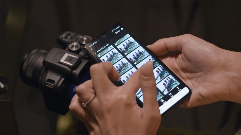 Hands holding a phone showing the Canon Camera Connect app. A Canon EOS R10 can be seen in the background.