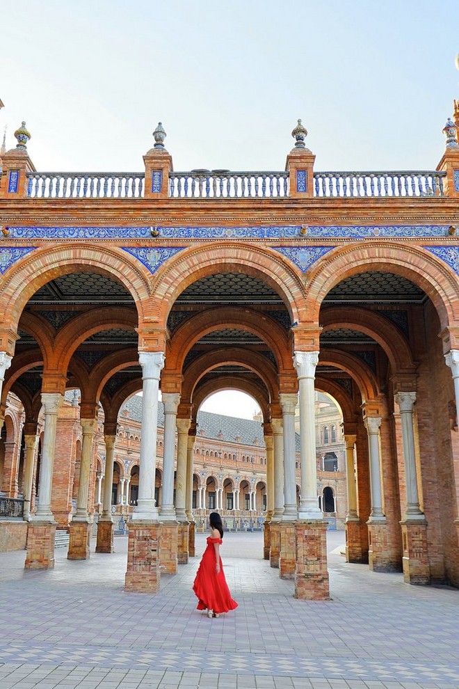 A woman in a red dress poses in front of a series of ornate archways.