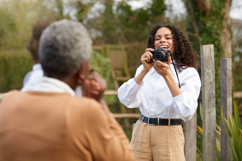 A person holds up a Canon EOS R100 camera to photograph two family members seen from behind.