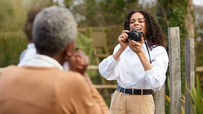 Osoba drží fotoaparát Canon EOS R100 a fotografuje dvoch členov rodiny pri pohľade zozadu.