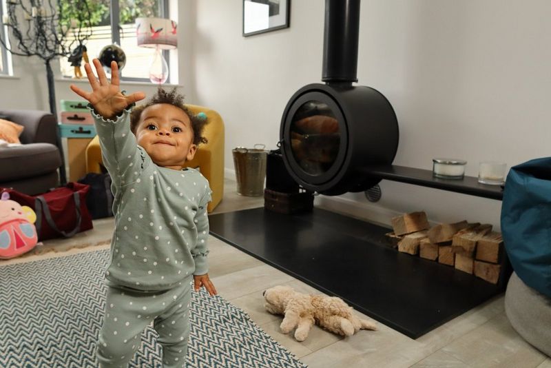 A black toddler is walking towards the camera with their hand held up high as if reaching for something.