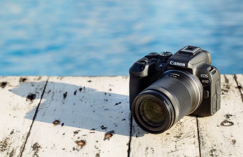 A Canon EOS R10 camera casts a shadow on a wooden jetty.