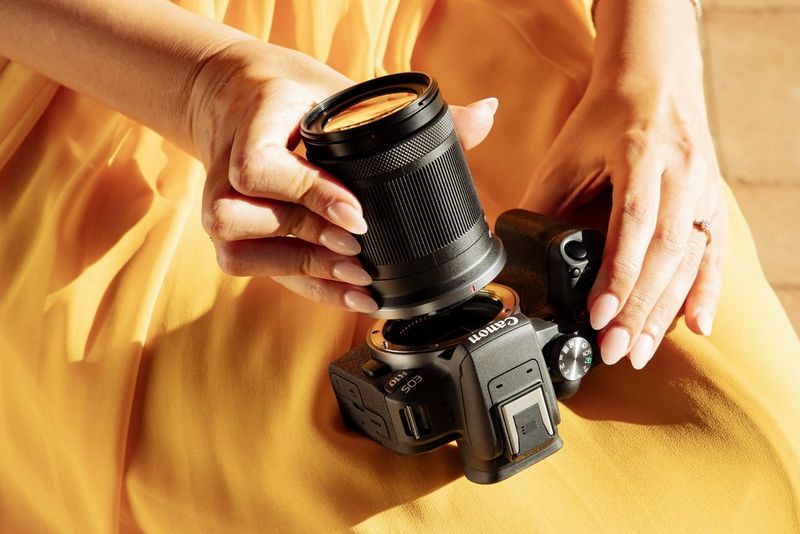 A person wearing a yellow dress attaches a Canon lens to a Canon EOS R10 camera.