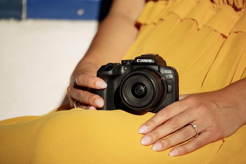 A Canon EOS R10 with RF-S 18-150mm F3.5-6.3 IS STM lens rests on the lap of a woman wearing a bright yellow dress. 