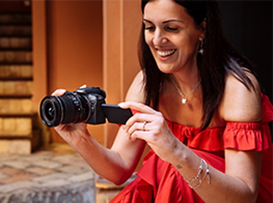 A woman wearing a red strapless dress crouches down to take a picture with a Canon EOS R10.