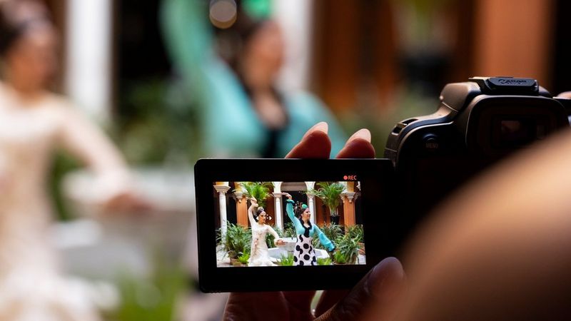 A view over the photographer's shoulder of the LCD screen of a Canon EOS R10, showing two flamenco dancers being filmed.