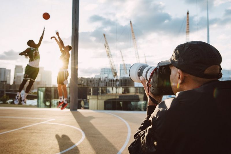 Le photographe Atiba Jefferson utilise le Canon EOS R1 pour photographier deux joueurs de basketball, avec leur ballon en plein ciel et le soleil rayonnant entre eux.