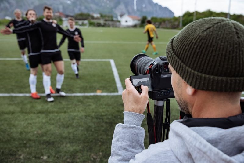 A videographer uses a Canon EOS R1 to film footballers on the pitch celebrating.