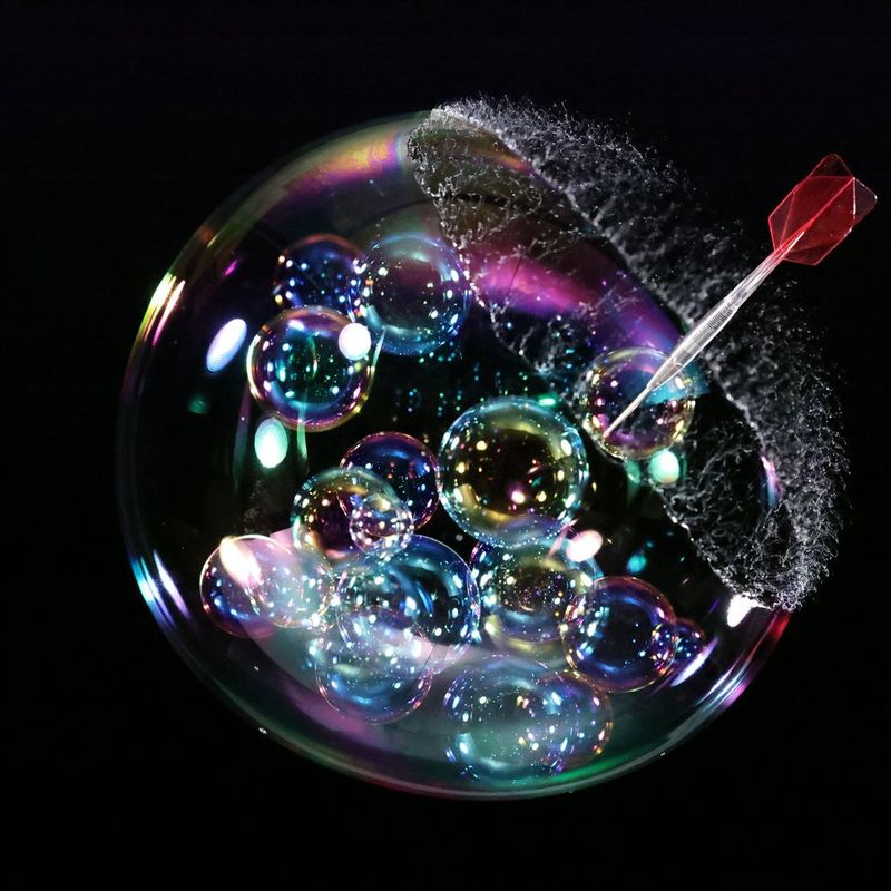 A dart captured at the moment it pierces a soap bubble, with the bubble just starting to burst.