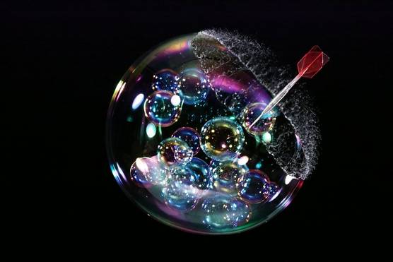 A dart captured at the moment it pierces a soap bubble, with the bubble just starting to burst.