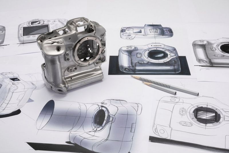 Металлическая основа корпуса Canon EOS R3 стоит на зарисовках чертежей; рядом лежат два карандаша.