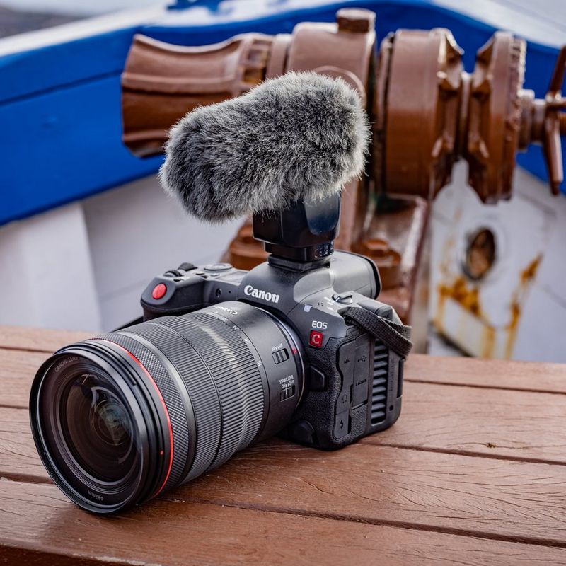 A Canon EOS R5 C, with a mic attached to it, sits on a wooden bench in the bow of a boat.
