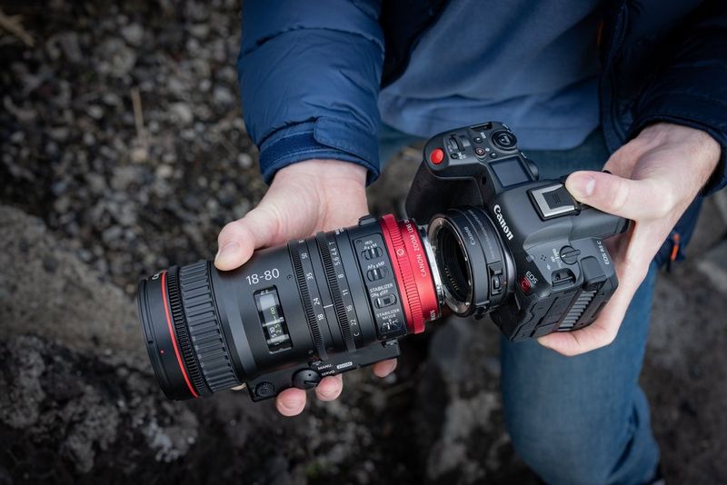 Hands fixing a lens to the Canon EOS R5 C hybrid camera.