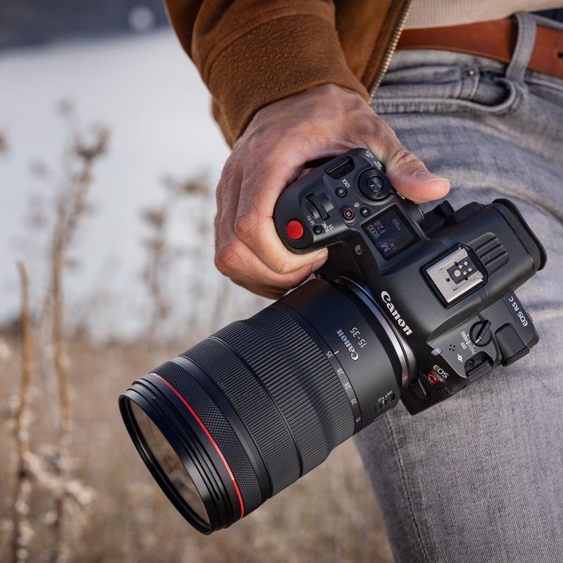 A man's hand holding a Canon EOS R5 C with a 15-35mm lens.