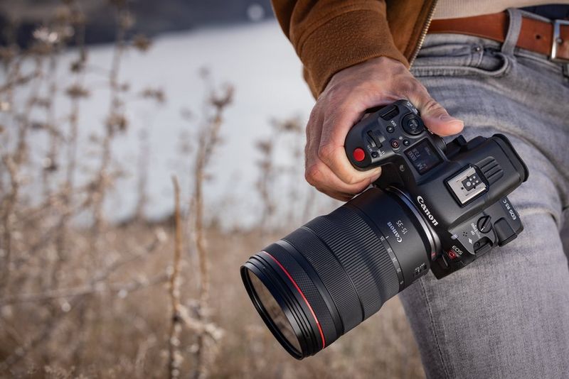 A man, shot so only his hand and waist is visible, holding a Canon EOS R5 C with a 15-35mm lens.