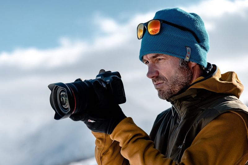 Un fotografo che indossa giacca, cappello e guanti invernali, con una fotocamera Canon EOS R5.