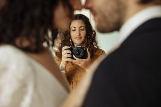 Photographer Alison Bounce looks at the rear screen of a Canon EOS R5 camera to capture a bride and groom as they embrace in the foreground.