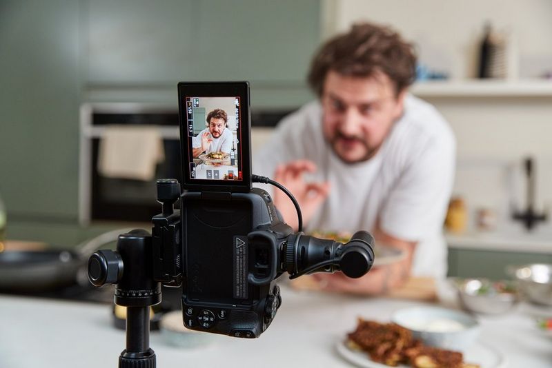 A Canon EOS R50, positioned on a tripod for vertical shooting, filming food influencer Martyn Odell in a kitchen.