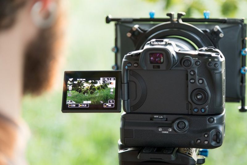 The rear of a Canon EOS R5 camera, mounted on a tripod for filming. 