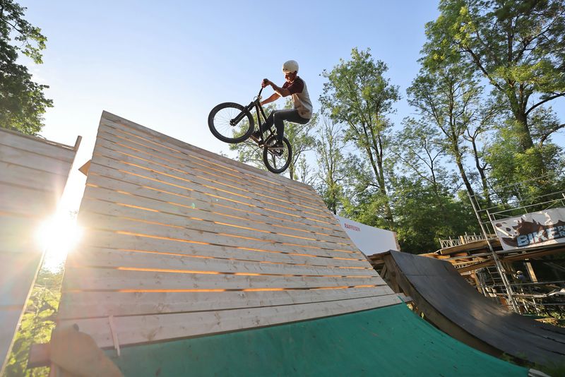 A mountain biker performs a stunt at the top of a curved wooden ramp.