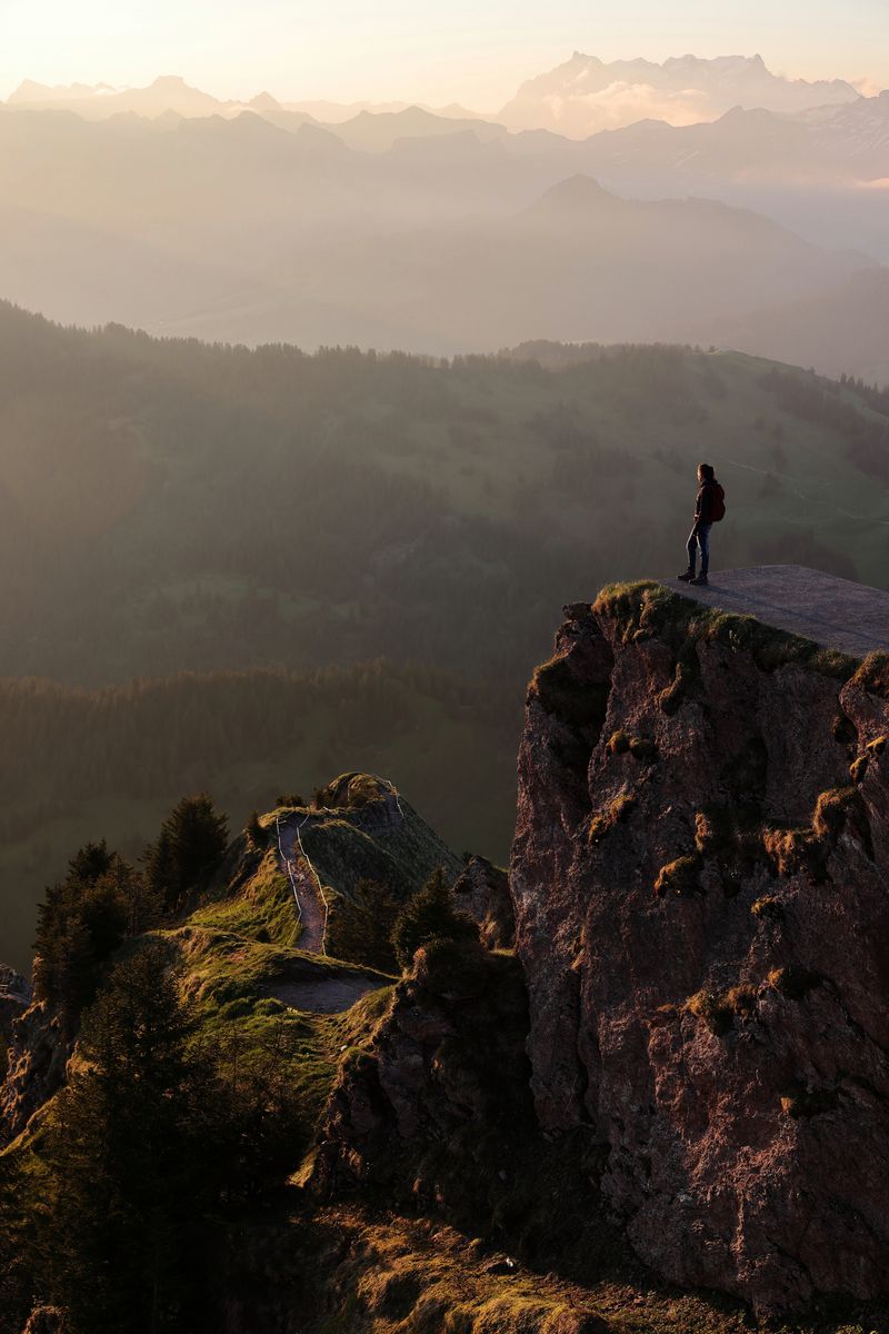 A woman stands on a rocky outcrop gazing at the mist-shrouded mountains in the distance.