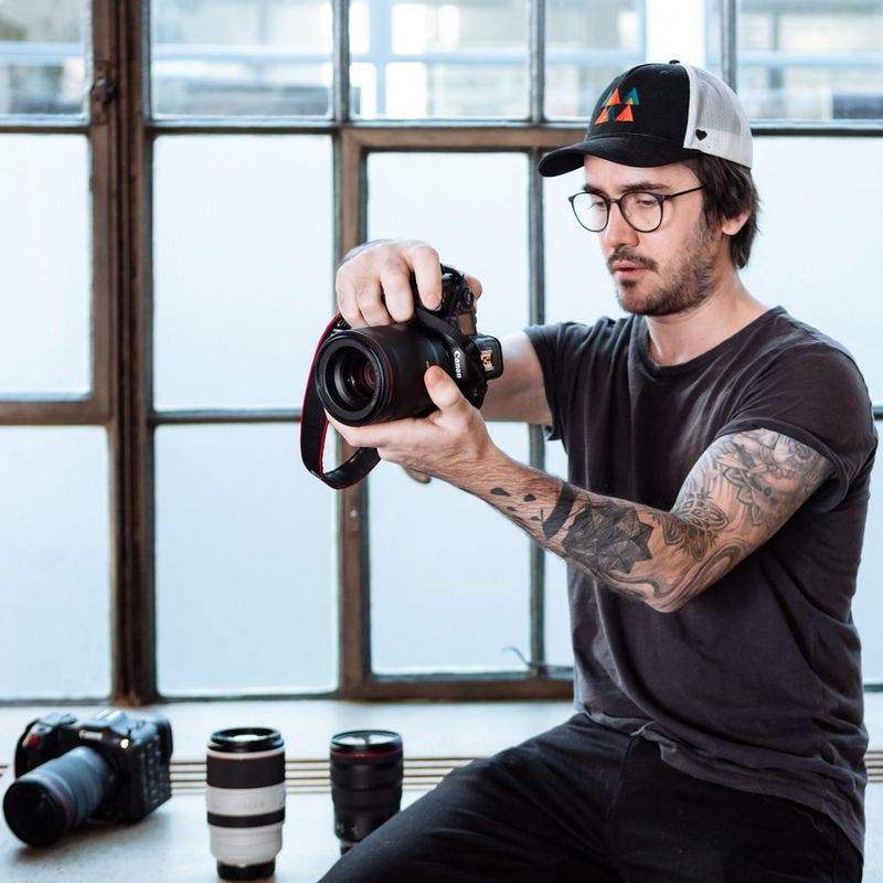 Steven Herteleer looks at the LCD screen of a Canon camera, another camera and two lenses on the surface next to him. 