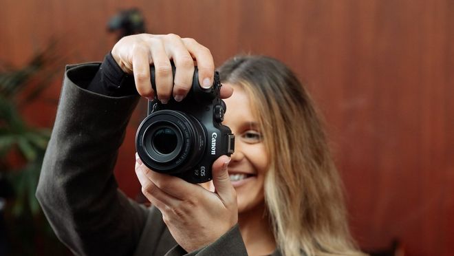 Creative portrait photographer Rosie Hardy smiles as she holds up a Canon EOS R7 and looks at its rear screen.
