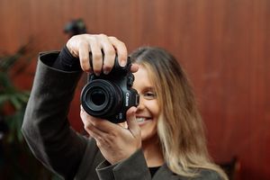 Die kreative Porträtfotografin Rosie Hardy lächelt, während sie eine Canon EOS R7 hochhält und das rückseitige Display dieser betrachtet.