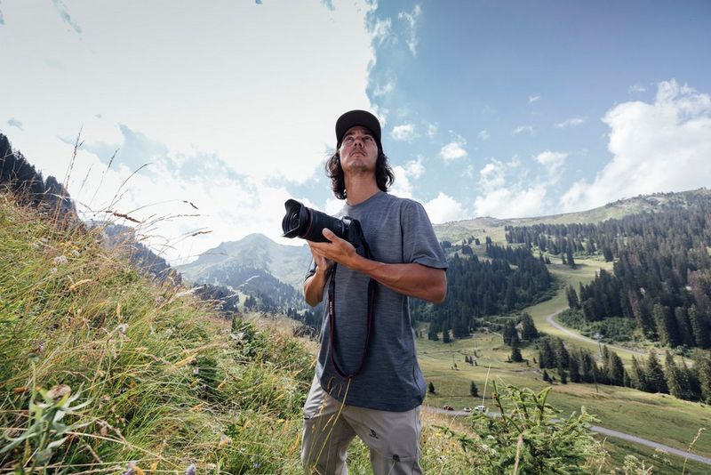 Teddy Morellec stands on a mountainside looking up at the sky and holding a Canon EOS R6 Mark II camera.
