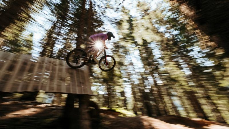 A mountain biker jumping through woods with a blurred background.