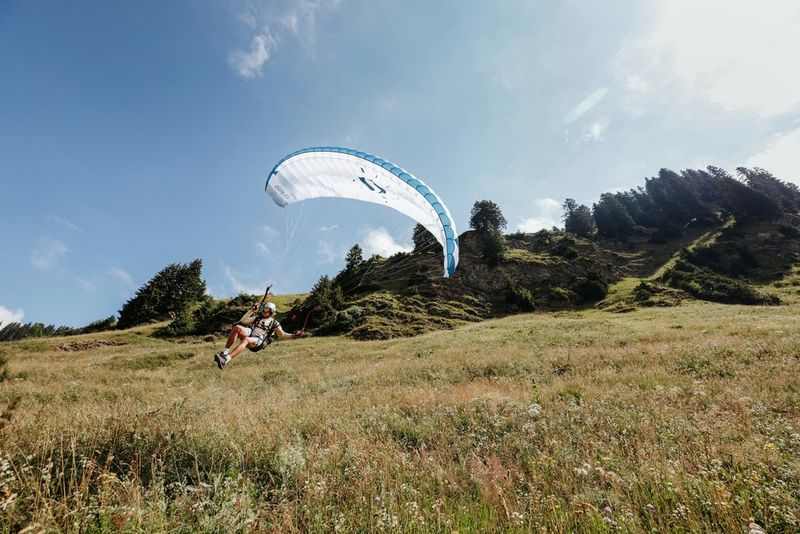 A speed rider with a white parachute landing on a grassy field.
