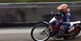 A person riding a dirt bike around a track, leaning the bike low to the ground, photographed using camera panning. © Richard Walch