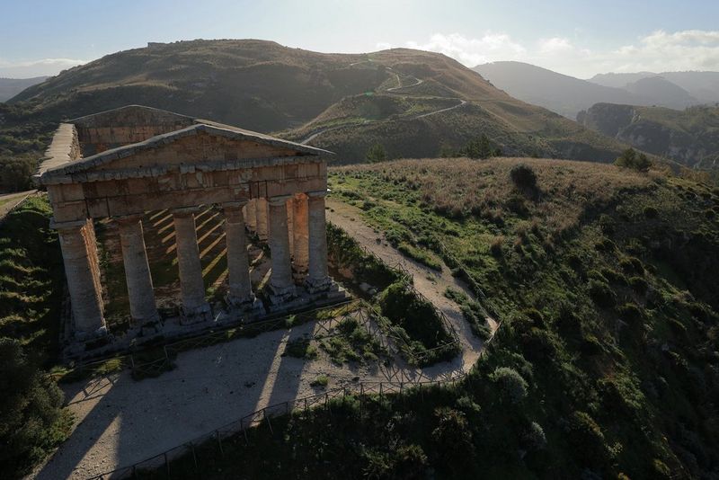 A hilltop temple casts long shadows on the ground as the sun sets behind it.