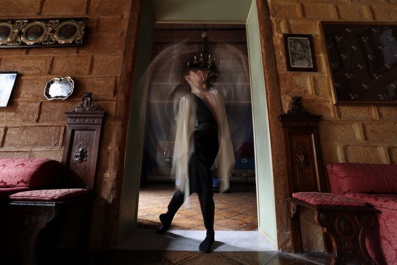 A dancer stands in a doorway of an ornately decorated room, arms blurred by motion.