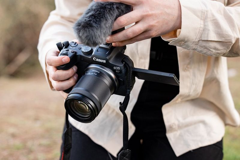 A close up of a person holding a Canon EOS R7 camera with a microphone attached to it.
