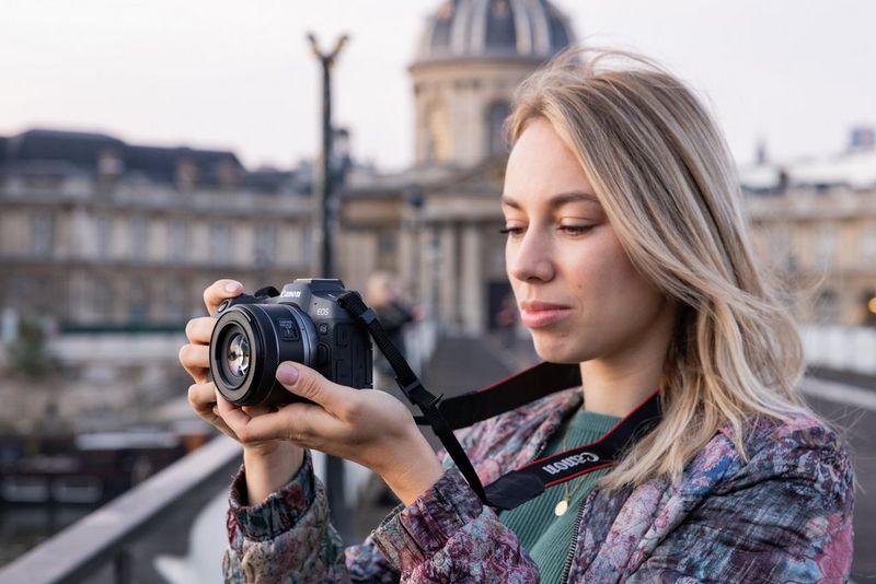 Alexandra Andreeva sujeta una EOS R8 de Canon, con un gran edificio detrás de ella desenfocado.
