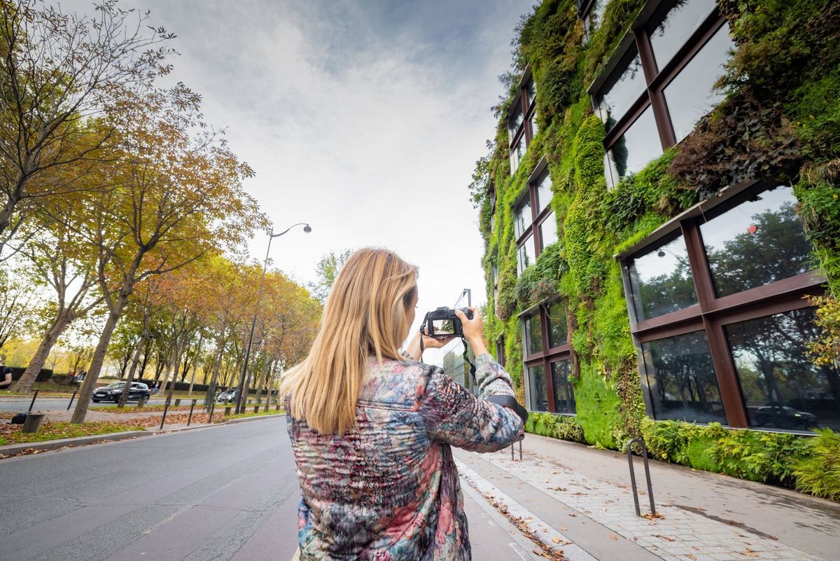 Photographer Alexandra Andreeva stands on a Paris street photographing an ivy-covered building with a Canon EOS R8.  