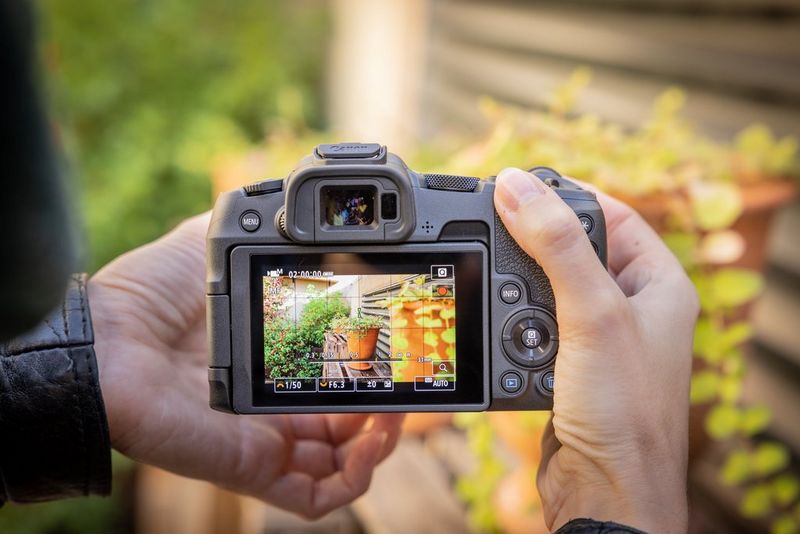 Человек держит в руках камеру Canon EOS R8; на заднем экране отображается функция помощи при фокусировке во время съемки видео.